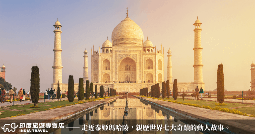 這張圖片呈現印度著名地標泰姬瑪哈陵(Taj Mahal)的正面全景。建築以白色大理石打造,配有圓頂與四座高塔,左右對稱地矗立於藍天與夕陽映照下。前方水池與花園反射建築輪廓,增添莊嚴寧靜氛圍。圖片下方搭配「印度旅遊專賣店」品牌標誌與行銷文案,強調這座世界七大奇蹟背後的動人愛情故事。