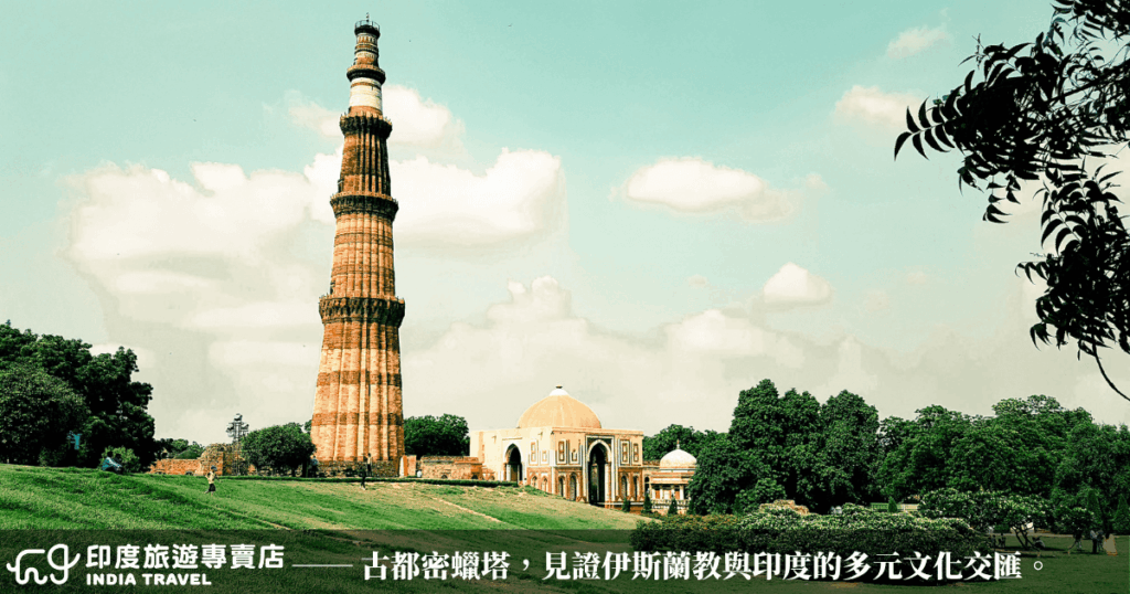 圖片清晰捕捉德里知名地標——古都密蠟塔(Qutub Minar)的完整塔身與周邊遺跡,塔身以紅砂岩打造,垂直線條與細膩雕刻展現伊斯蘭建築風格的華麗與秩序。前景草地遼闊,襯托出塔的高聳與孤絕,右側枝葉自然入鏡,增添一分靜謐氣息。遠處的圓頂建築是庫瓦特伊斯蘭清真寺(Quwwat-ul-Islam),象徵伊斯蘭教初入印度時的重要足跡。