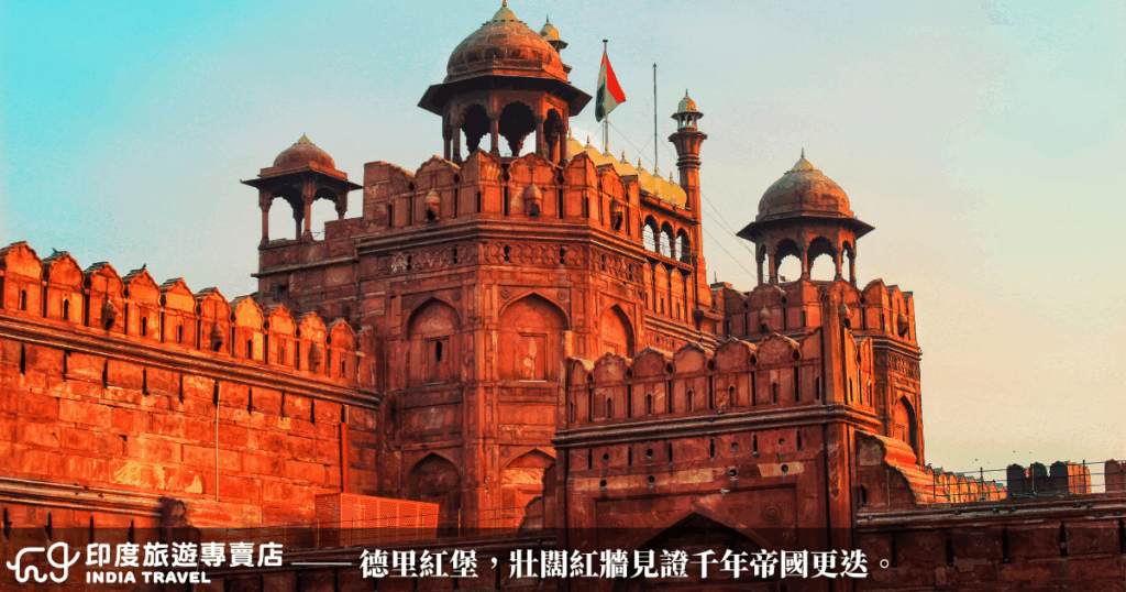 這張照片呈現德里紅堡（Red Fort）的主牆與城樓建築，夕陽灑落在紅砂岩外牆上，映出一片溫暖橘紅色調，凸顯出莫臥兒王朝的建築宏偉與歷史厚重感。紅堡是德里最具代表性的世界文化遺產之一，也是昔日帝國的權力中心。圖片中可見堡壘頂端飄揚著印度國旗，象徵歷史與現代的交會。整體構圖強調建築線條與對稱之美。
