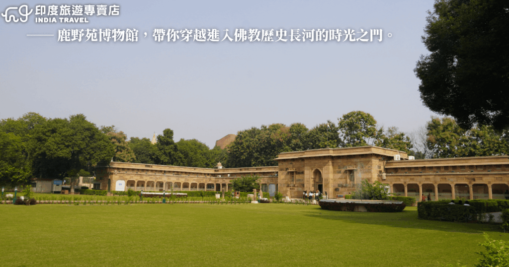 圖中為印度瓦拉納西（Varanasi）近郊的鹿野苑（Sarnath）博物館主建築，坐落於綠意盎然的庭園中，遠方可見林木掩映下的古塔遺跡。圖片上方搭配文字「鹿野苑博物館，帶你穿越進入佛教歷史長河的時光之門」，象徵此地是佛陀初轉法輪之地，也是理解佛教發展的重要起點。整體構圖穩重寧靜。