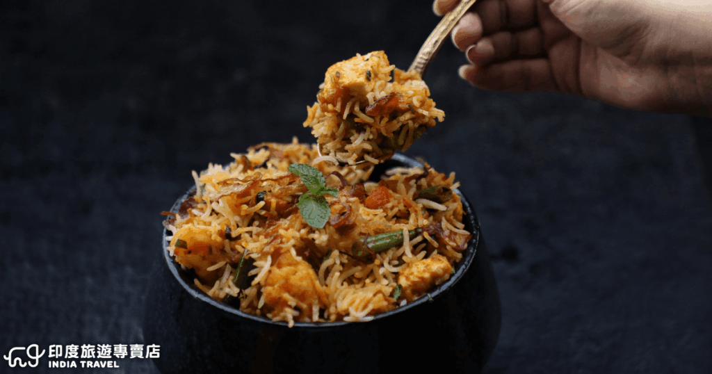 這張圖片呈現印度經典料理「Biryani」，碗中盛裝著香氣四溢的長米，搭配蔬菜、香料與鮮嫩的起司塊（Paneer）。表面點綴著薄荷葉與酥脆炸洋蔥，散發出濃郁的辛香氣息。Biryani 是印度家喻戶曉的美食之一，不論節慶、婚宴或日常用餐都常見它的身影，象徵著印度飲食文化中對香料運用的極致藝術與熱情。