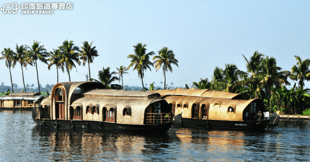 畫面展示印度喀拉拉邦(Kerala)的傳統屋船 Kettuvallam,整艘船以竹子、椰纖與天然材料編織而成,漂浮於寧靜的回水區(Backwaters)。船隻造型獨特,帶有拱形的茅草屋頂與木製窗框,背後是一排搖曳的椰子樹與藍天,映照在清澈水面上,營造悠閒而異國風情的氛圍。這類屋船常被用於旅遊觀光,提供住宿、餐飲與慢遊體驗,是到訪喀拉拉必不可少的文化象徵與旅遊亮點。