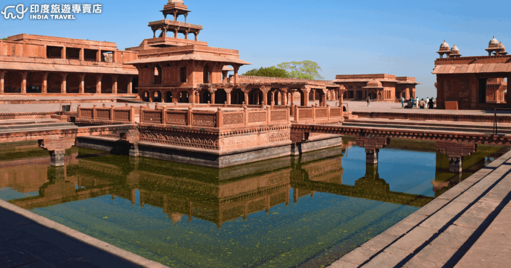 畫面展示印度北方邦的世界文化遺產——法塔赫普西克里(Fatehpur Sikri)。紅砂岩建築環繞水池而立,中央的精緻宮殿與四周迴廊倒映在池水之中,展現莫臥兒王朝建築工藝的對稱與華麗。這裡曾是皇帝阿克巴短暫的首都,如今成為遊客必訪的歷史景點。